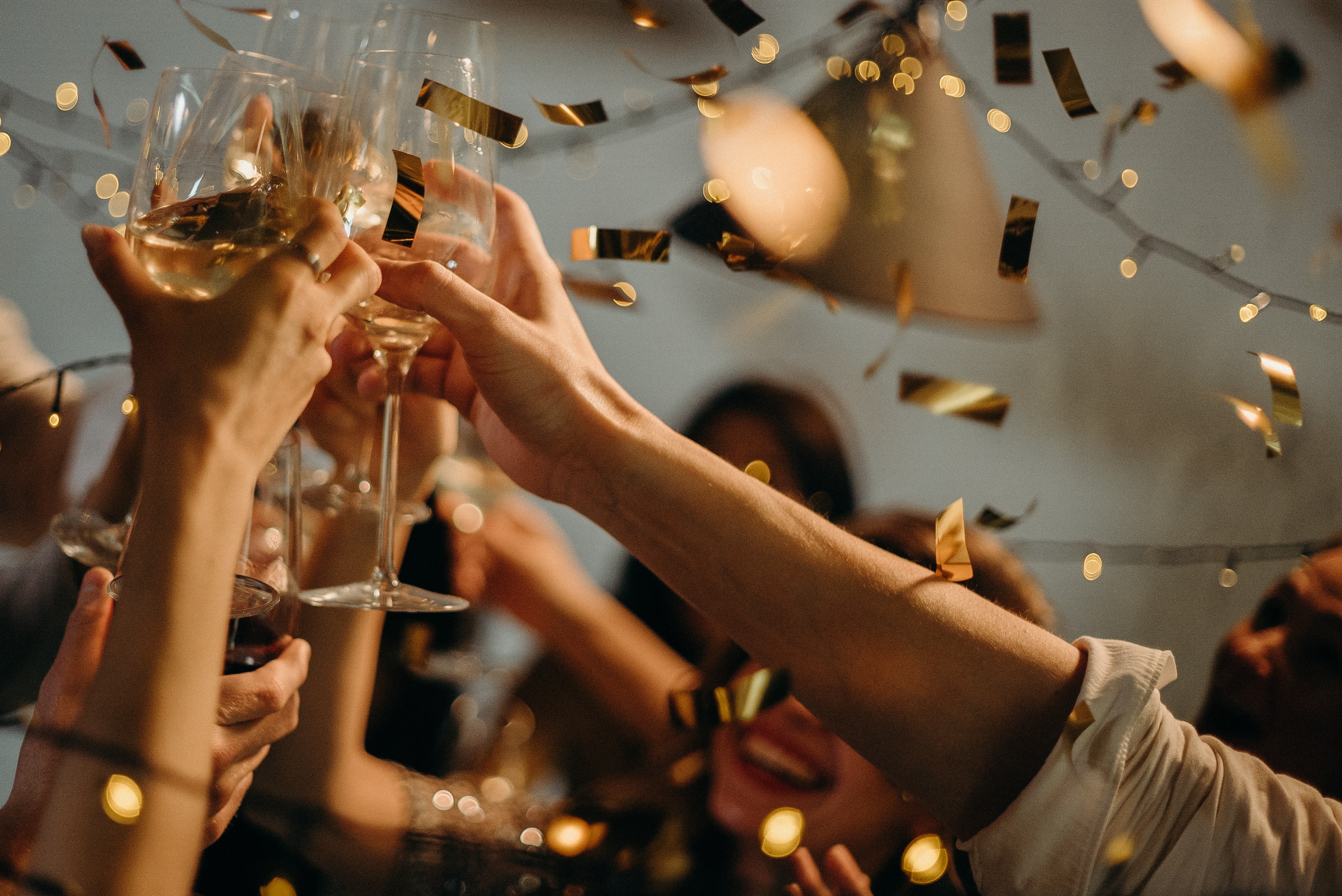 Photo of people holding up Champagne glasses as confetti falls on New Years